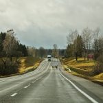 A straight highway with trucks amidst overcast skies and surrounding fields.